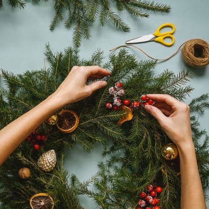 Christmas composition. Woman making handmade christmas wreath. Top view, flat lay. Blue background, fir branches, berries, orange and apple slices, rope and scissors. Step 2.